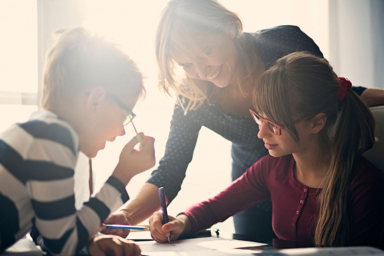 A woman and two children are working on a piece of paper. The woman is smiling and the children are focused on their work.