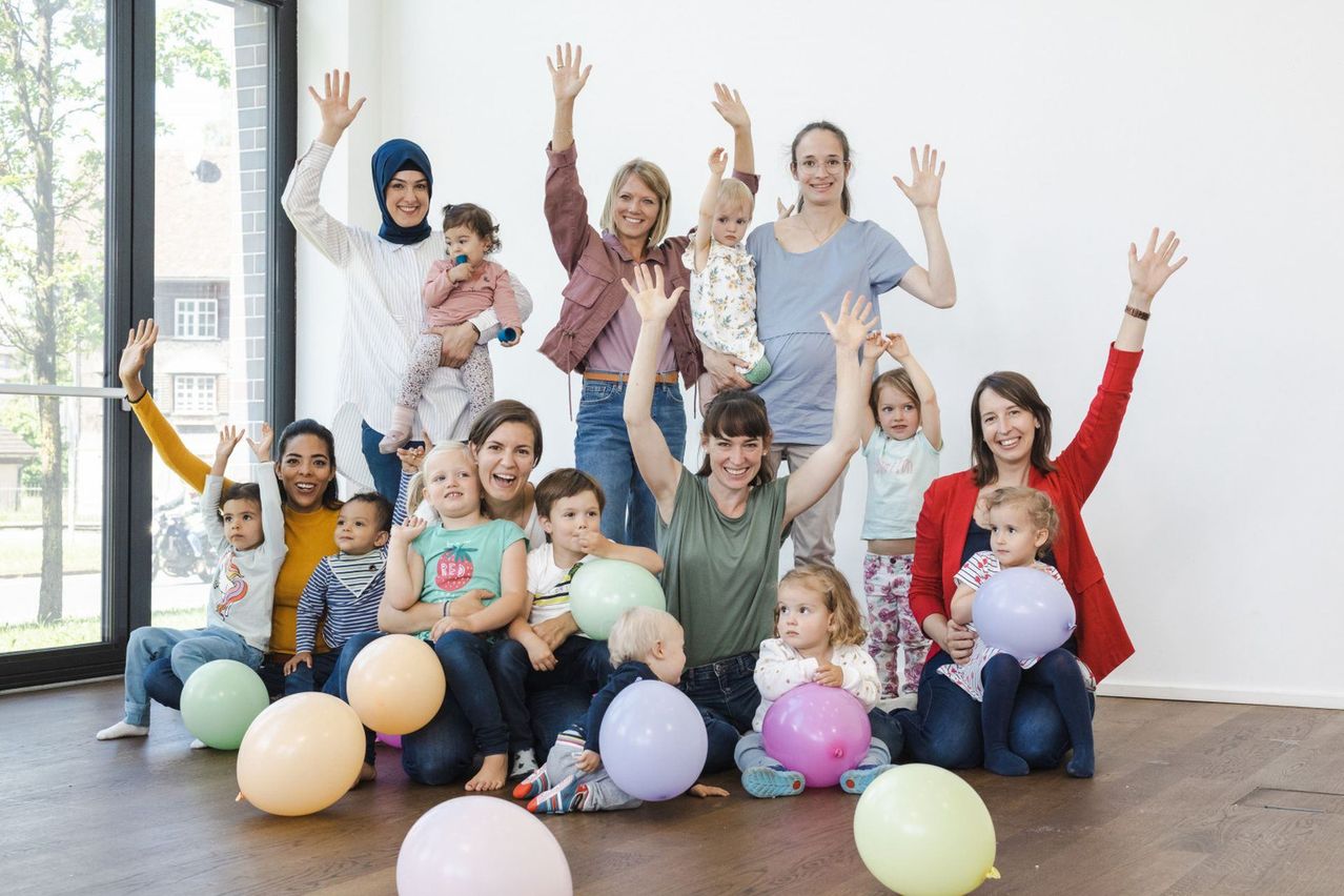 Eine Gruppe von Frauen und Kindern lächelt und posiert mit Luftballons für ein Foto in einem Raum.