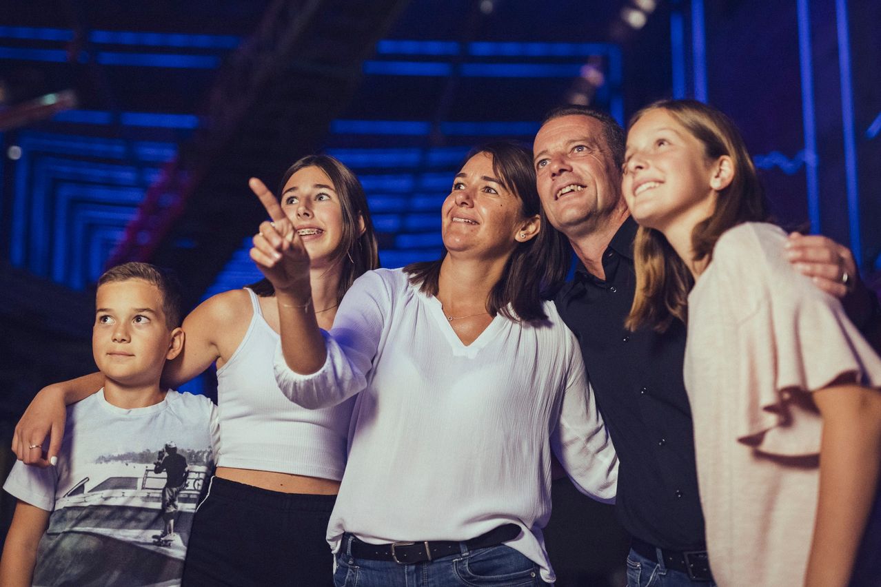 Eine vierköpfige Familie, zwei Frauen und zwei Männer, lächelt und posiert für ein Foto bei einer Veranstaltung. Die Frau auf der linken Seite zeigt auf etwas, während die anderen zuschauen.