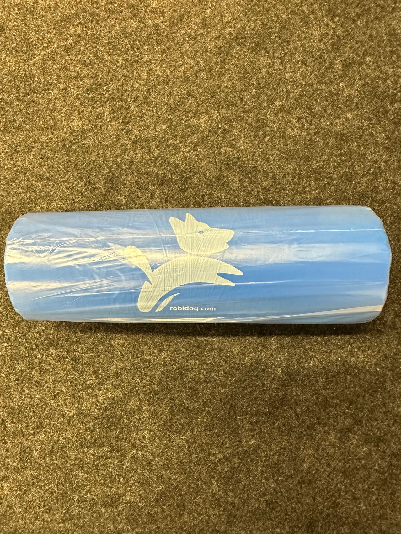 A blue yoga mat with a white dog logo is wrapped in plastic on a brown carpet.