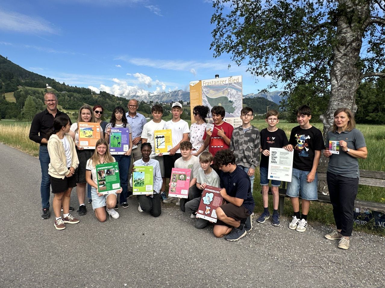 Gruppe von Menschen, die Plakate in einem Foto halten, steht in einer Reihe auf einem Feld mit Bergen im Hintergrund.