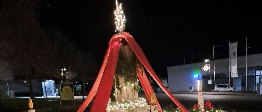 Ein Weihnachtskranz mit roten Bändern und Lichtern auf einer Kopfsteinpflasterstraße in der Nacht.