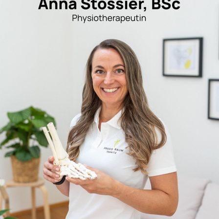 Eine Frau lächelt und hält ein Knochenmodell in der Hand, während sie in einem Raum steht. Sie trägt ein weißes Hemd mit Text. Dahinter steht eine Topfpflanze und ein gerahmtes Bild.