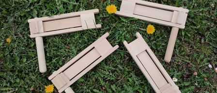 Vier Holzteile eines Musikinstruments liegen auf einem grünen Rasen, jeweils mit einer gelben Blume in der Nähe.