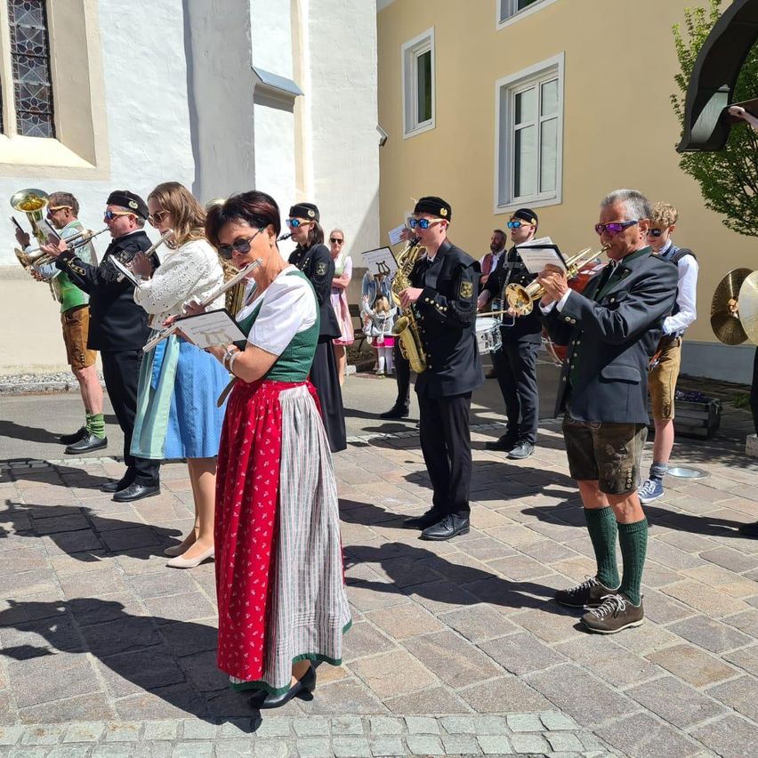 Eine Gruppe von Musikern in traditioneller Kleidung steht auf einem gepflasterten Platz und hält verschiedene Instrumente wie Trompeten und Tuben.