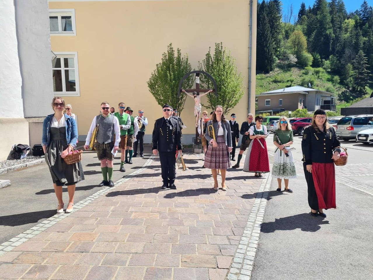 Eine Gruppe von Menschen in traditioneller Kleidung steht vor einer Kirche mit einem Kreuz. Sie nehmen wahrscheinlich an einer Zeremonie oder Veranstaltung teil.