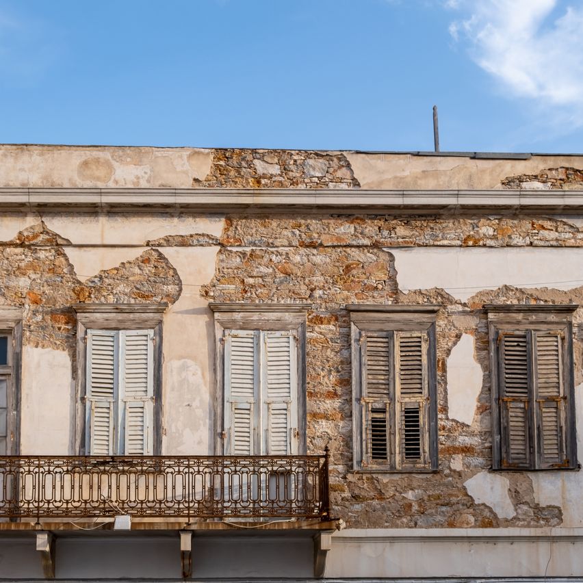 Ein altes Steingebäude mit abblätternder Farbe, einem Balkon mit rostigen Geländern und vier geschlossenen Fenstern.