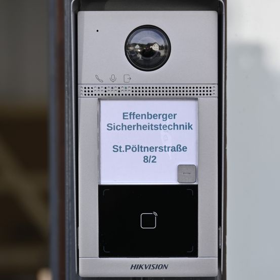 Ein Nahaufnahme eines Hikvision-Videotürgongs mit einer Sicherheitskamera, einem Mikrofonsymbol und einem kleinen Bildschirm, auf dem die Adresse 'Effenberger Sicherheitstechnik, St. Pöltnerstraße 8/2' steht.