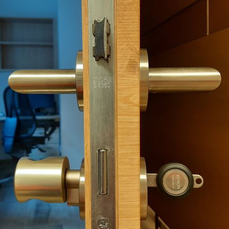 Eine Nahaufnahme eines messingfarbenen Türgriffs und Schlosses mit eingelegtem Schlüssel. Das Schloss trägt die Aufschrift "ASSA ABLOY" und der Griff hat eine silberne Oberfläche.