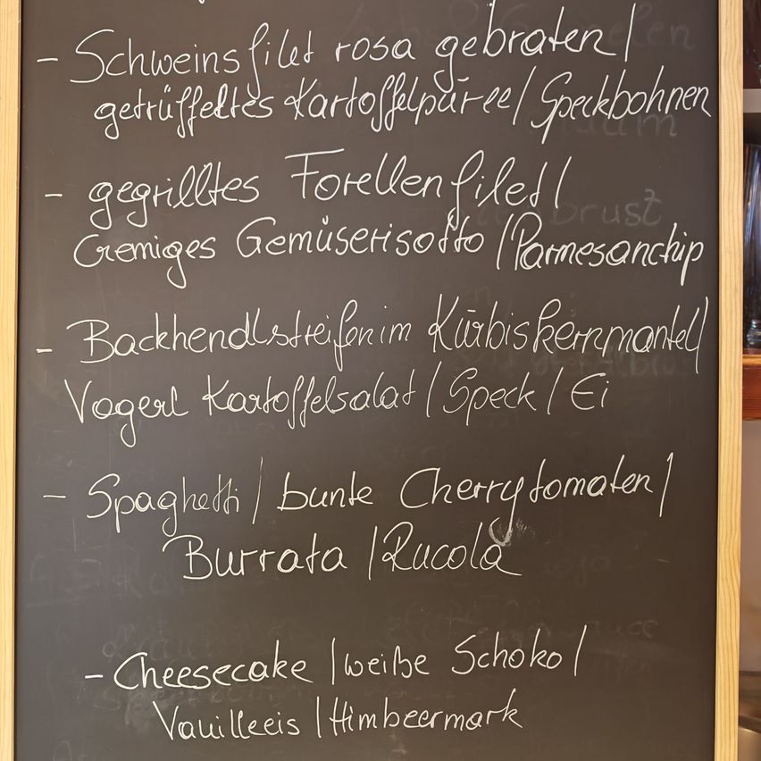 Ein Tafelmenü auf einer Tafel bietet verschiedene Gerichte wie gebratenes Schweinefilet, Forellenfilet, Hühnersalat, Spaghetti und Käsekuchen an.