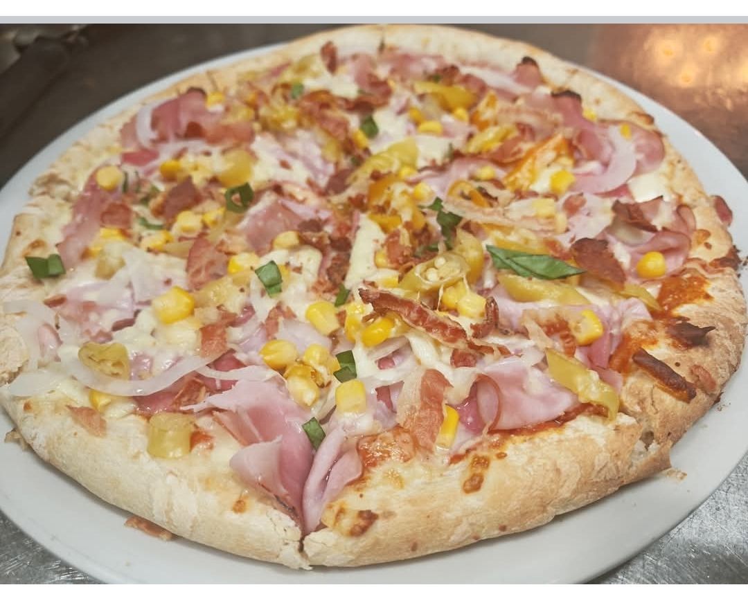 Eine ganze Pizza mit Schinken, Mais, Käse und Zwiebeln auf einem weißen Teller, bereit zum Verzehr.