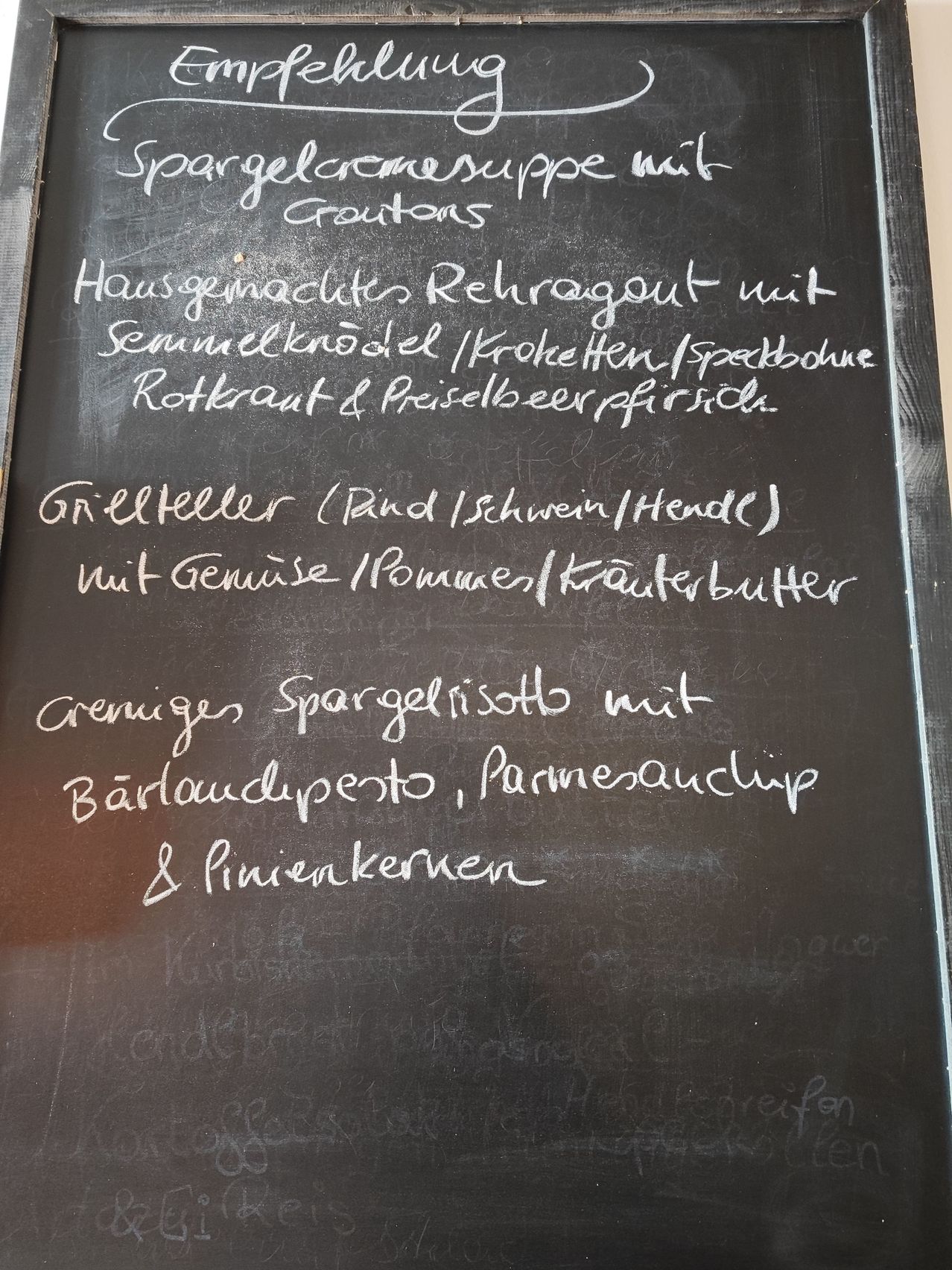 Eine Kreidetafel mit hausgemachten Gerichten wie Spargelsuppe, gegrilltem Hähnchen und Spargelrisotto mit verschiedenen Toppings.