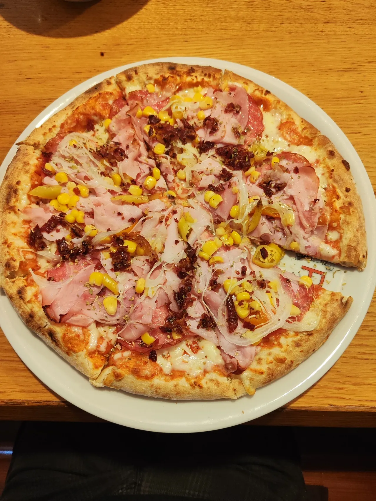 Eine Pizza mit verschiedenen Belägen wie Schinken, Mais und Zwiebeln auf einem Holztisch.