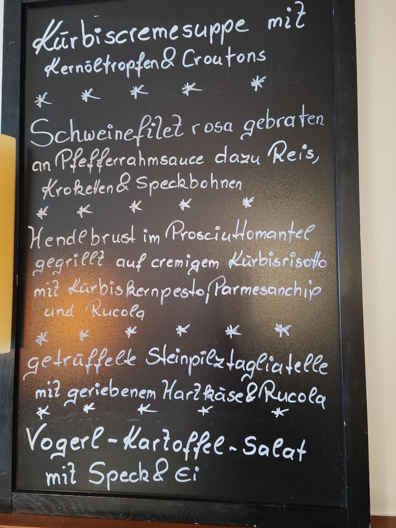 Ein schwarzes Kreidetafel-Menü mit verschiedenen Gerichten wie Schweinefilet mit Pfefferrahmsauce, Hähnchenbrust mit Prosciutto und trüffelnudeln.