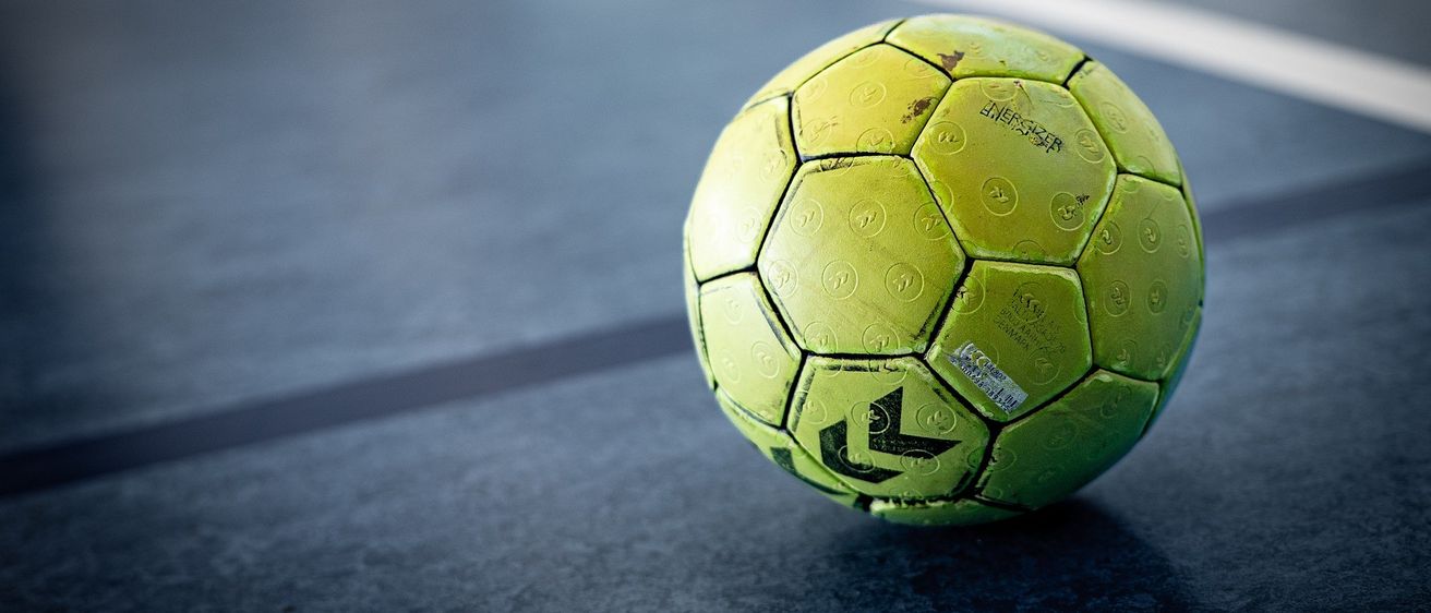 Eine Nahaufnahme eines gelben Fußballs mit schwarzen Markierungen und einem kleinen Aufkleber auf einem Spielfeld.