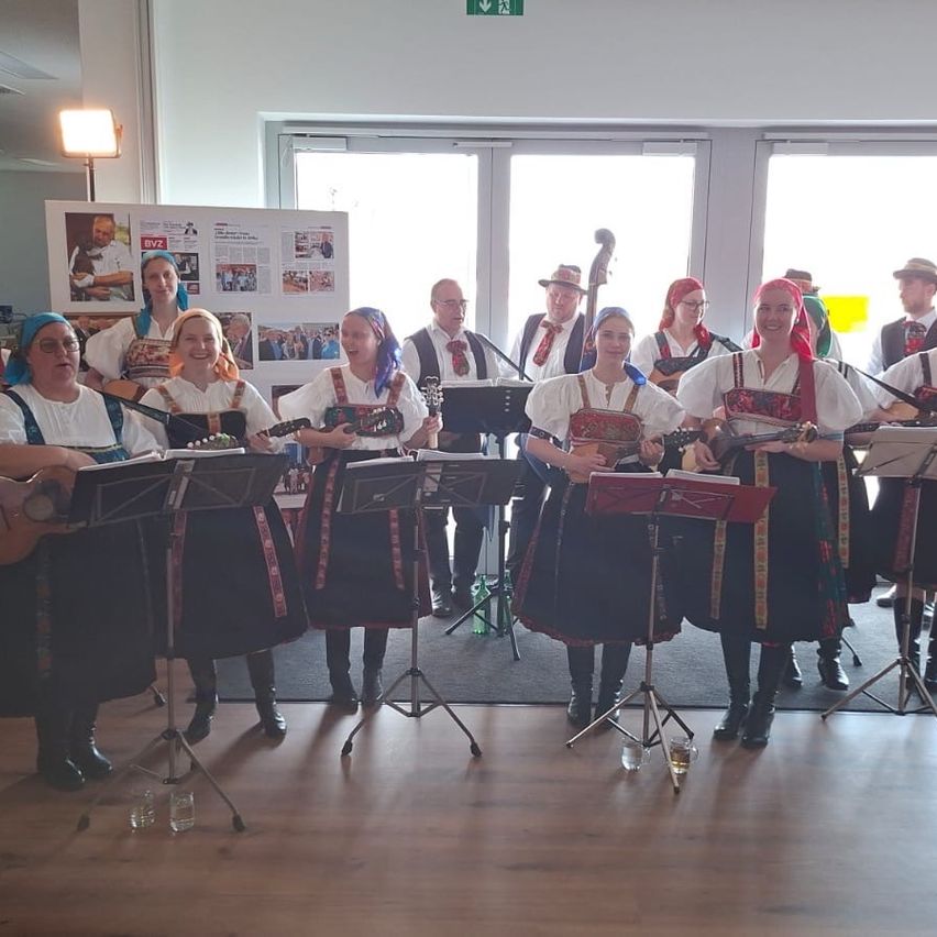 Eine Gruppe von Musikern in traditioneller Kleidung spielt Saiteninstrumente in einem Raum mit weißen Wänden und Holzböden.