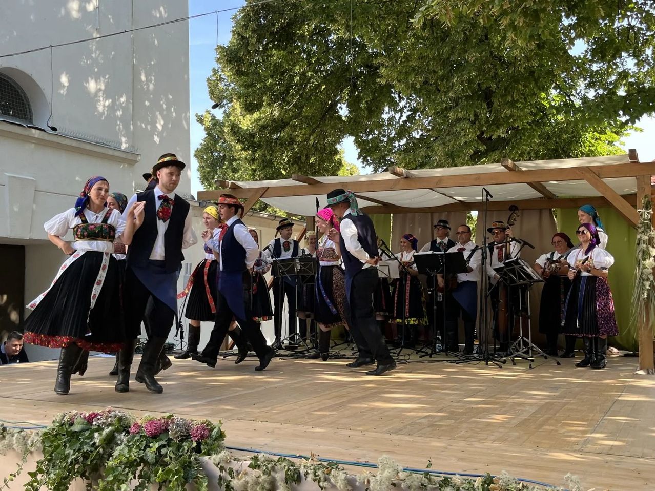 A group of people in traditional costumes dance on a stage with a band playing behind them.