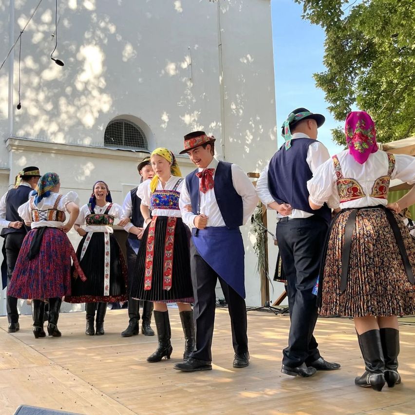 A group of people in traditional costumes are performing a dance on a wooden stage in front of a building.