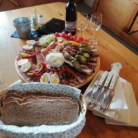 Ein Holztisch mit einem Charcuterie-Brett, Weingläsern, einer Flasche Wein und einem Korb mit Brot.