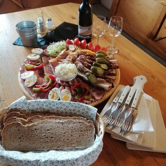 Ein Holztisch mit einem Charcuterie-Brett, Weingläsern, einer Flasche Wein und einem Korb mit Brot.