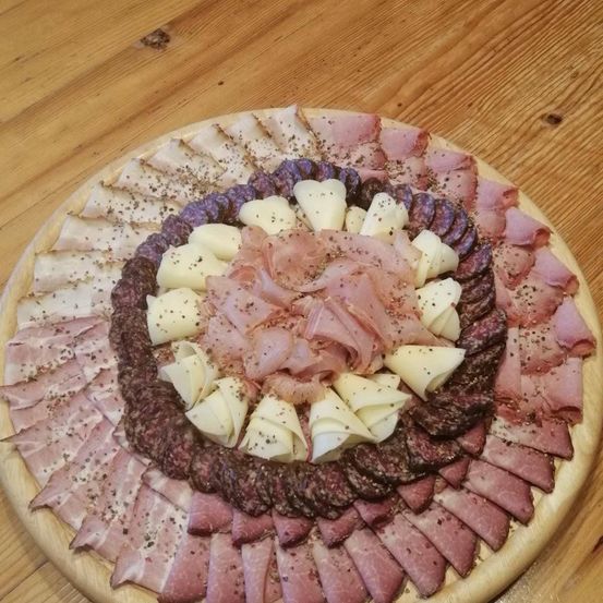 Ein Holzbrett zeigt eine kreisförmige Anordnung verschiedener Fleisch- und Käsesorten, darunter Schinken-, Salami- und Käsescheiben.