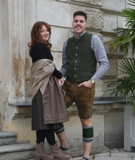 Ein Mann und eine Frau stehen auf den Stufen vor einem Gebäude. Sie lächeln beide und sehen in die Kamera. Der Mann trägt eine Uhr.