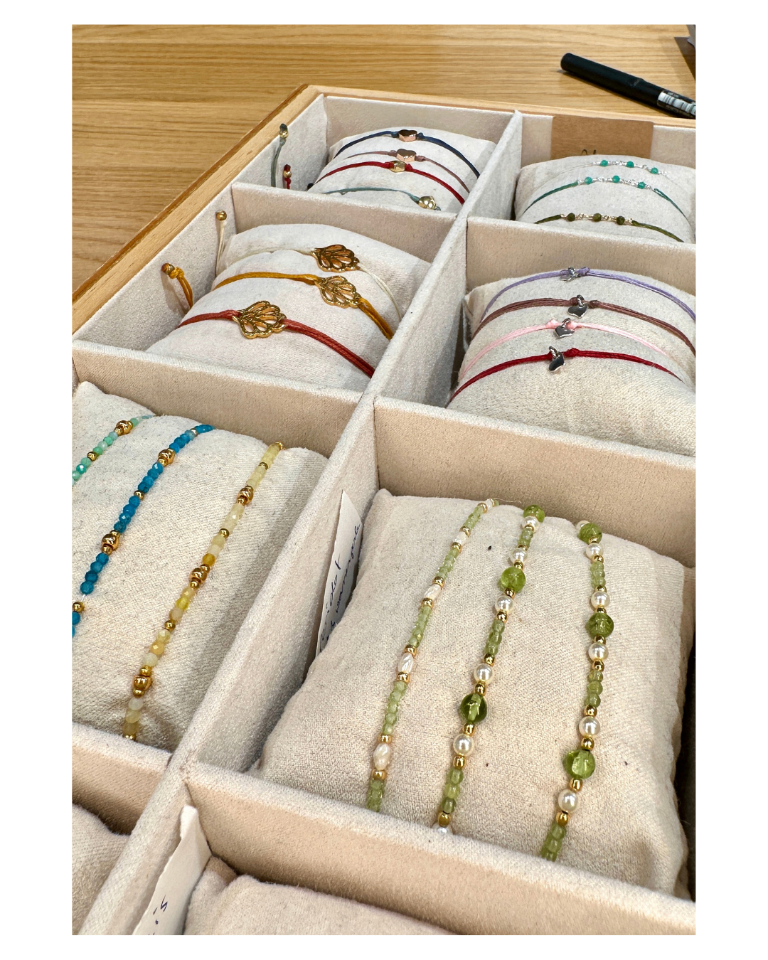 Eine Holzkiste ist in mehrere Fächer unterteilt. Jedes Fach hat ein Kissen mit einem Armband darauf. Die Armbänder sind in verschiedenen Farben und Stilen.