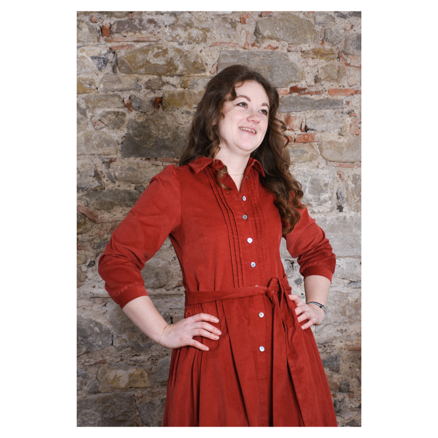 Eine Frau in einem roten Kleid steht vor einer Ziegelwand, lächelt und posiert für ein Foto.