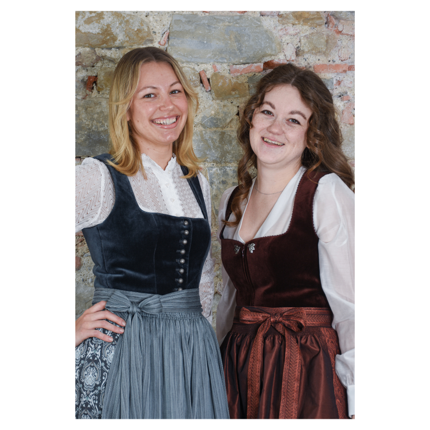 Zwei Frauen stehen nebeneinander und posieren für ein Foto. Sie tragen traditionelle Kleidung.