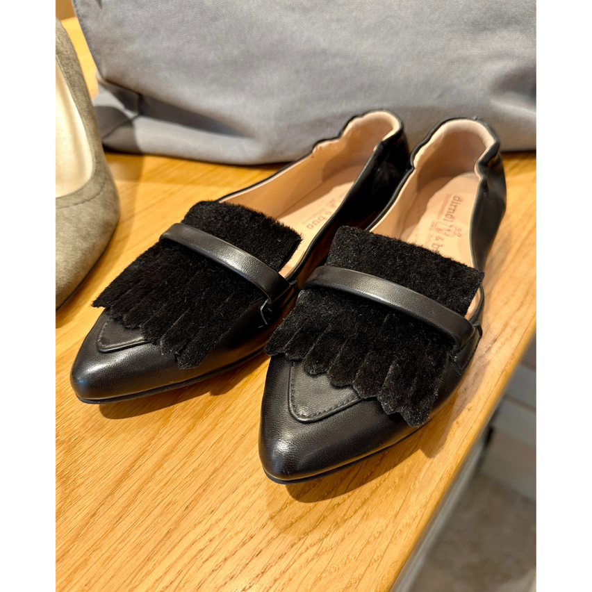 Ein Paar schwarze Lederschuhe mit Fransen auf einem Holztisch.