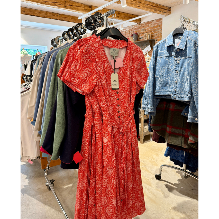 Ein rotes gemustertes Kleid hängt an einem Kleiderständer neben anderen Kleidungsstücken in einem Geschäft.