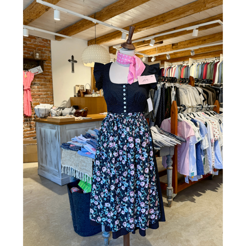 A mannequin wearing a floral dress with a pink scarf and a price tag is displayed in a clothing store.