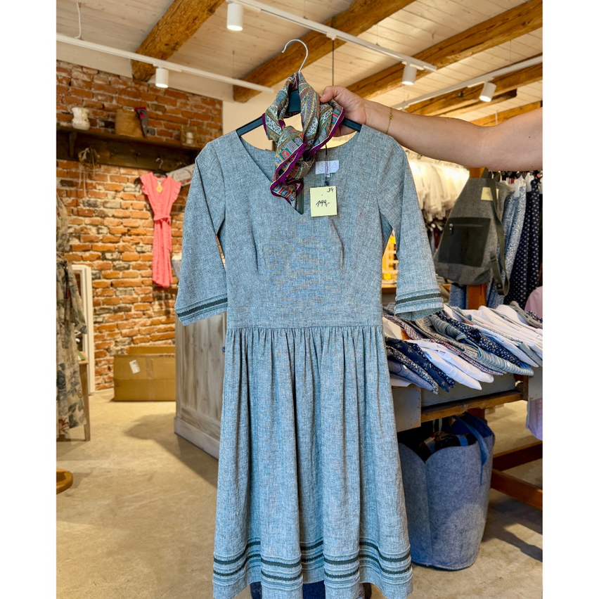 A light blue dress with a scarf around its neck is hanging on a hanger in a clothing store.