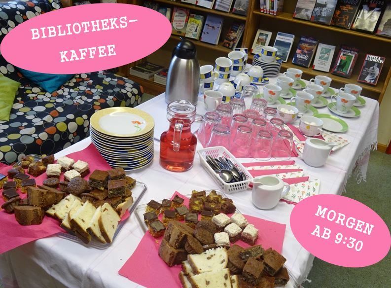 A table filled with various desserts, plates, cups, and a pitcher of juice. A sign reads 'Bibliotheks-Kaffee' and another sign reads 'Morgen ab 9:30.'