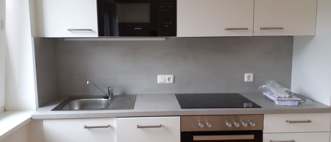 Eine moderne Küche mit weißen Schränken, einer schwarzen Mikrowelle, einem Waschbecken mit Wasserhahn und einem Gasherd mit Ofen.