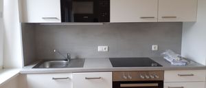 Eine moderne Küche mit weißen Schränken, einer schwarzen Mikrowelle, einem Waschbecken mit Wasserhahn und einem Gasherd mit Ofen.