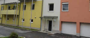 Ein dreistöckiges Mehrfamilienhaus mit gelben, weißen und orangefarbenen Wänden. Es hat einen Balkon im zweiten Stock, ein weißes Auto vor dem Haus und zwei Garagen.