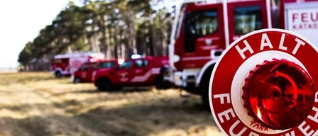 Ein roter Feuerwehrwagen mit dem Wort 'FEUER' auf einem roten Alarmknopf steht auf einem Feld.