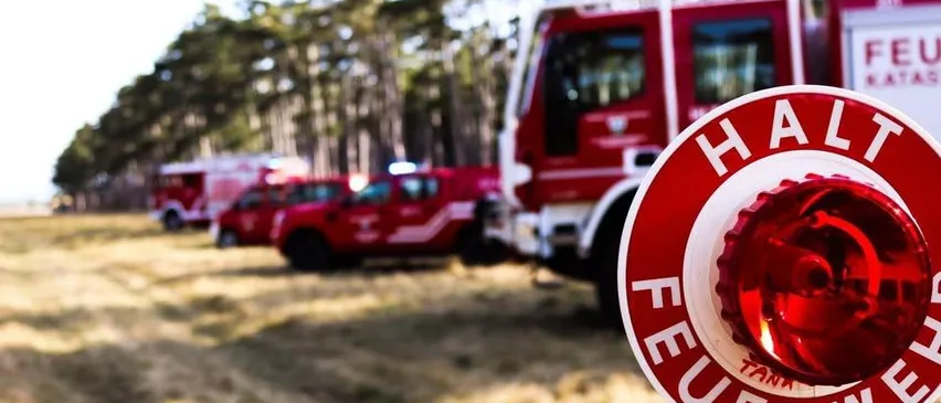 Ein roter Feuerwehrwagen mit dem Wort 'FEUER' auf einem roten Alarmknopf steht auf einem Feld.
