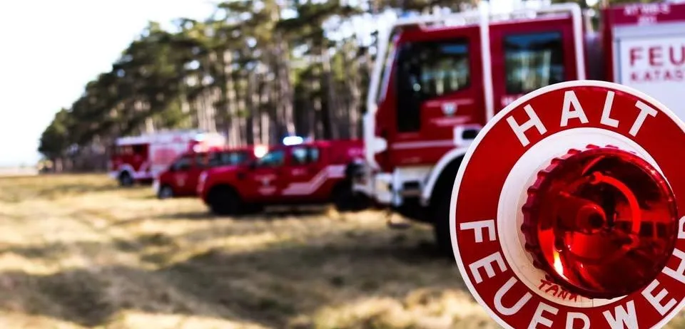 Ein roter Feuerwehrwagen mit dem Wort 'FEUER' auf einem roten Alarmknopf steht auf einem Feld.