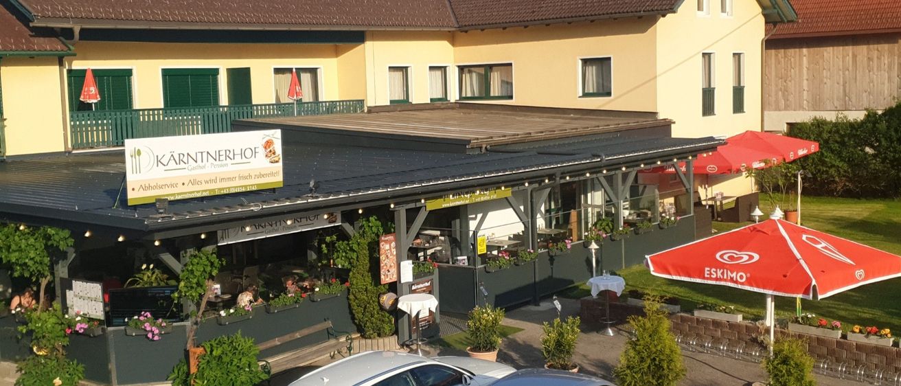 Ein Restaurant mit braunem Dach und gelben Wänden. Es hat einen Blick auf einen Berg und ein roter Regenschirm steht draußen. Es gibt auch Pflanzen und ein Auto, das vor dem Gebäude geparkt ist.