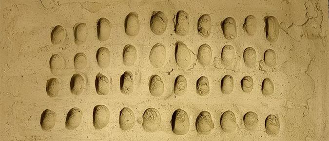 Eine Nahaufnahme einer sandigen Oberfläche mit zahlreichen kleinen, ovalen Abdrücken, die in Reihen angeordnet sind, möglicherweise ein Muster oder eine alte Schrift darstellen.