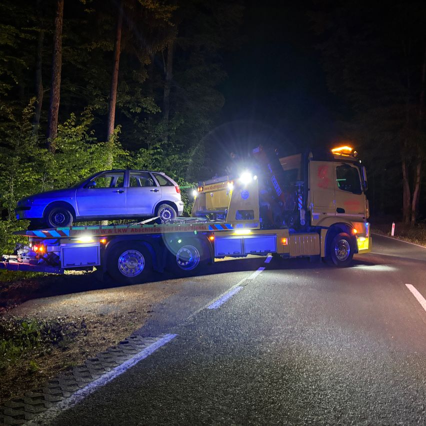 Ein Abschleppwagen mit eingeschalteten Scheinwerfern zieht ein blaues Auto nachts von der Straße.