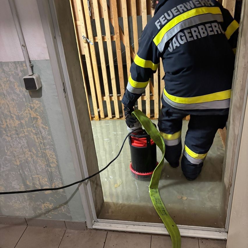 Ein Feuerwehrmann aus Jagerberger pumpt Wasser aus einem überfluteten Raum mit einer Tauchpumpe. Der Raum hat geflieste Böden.