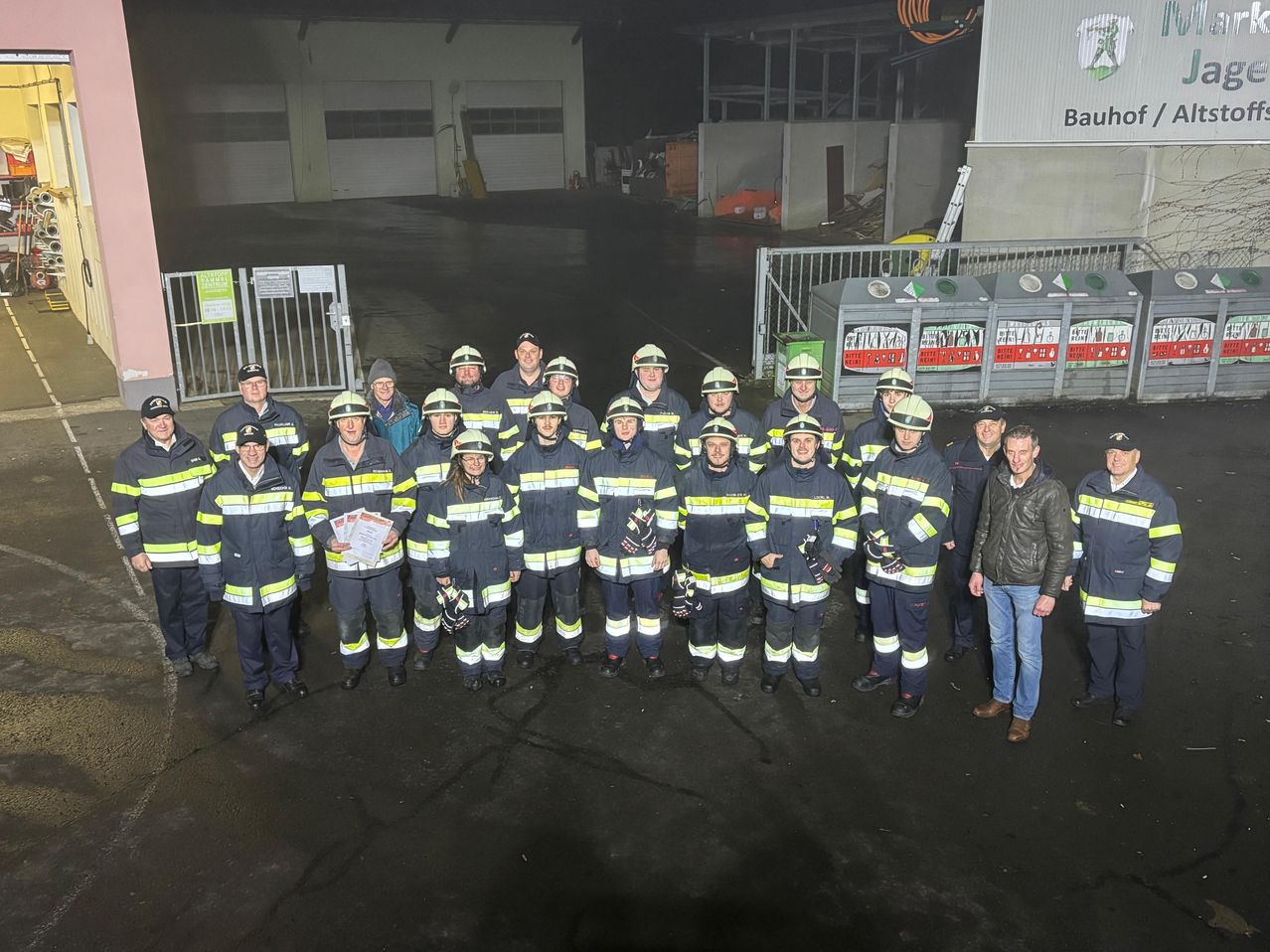 Eine Gruppe von Feuerwehrleuten in Uniform steht vor einem Gebäude mit dem Schriftzug 'BauL'. Sie posieren für ein Foto.
