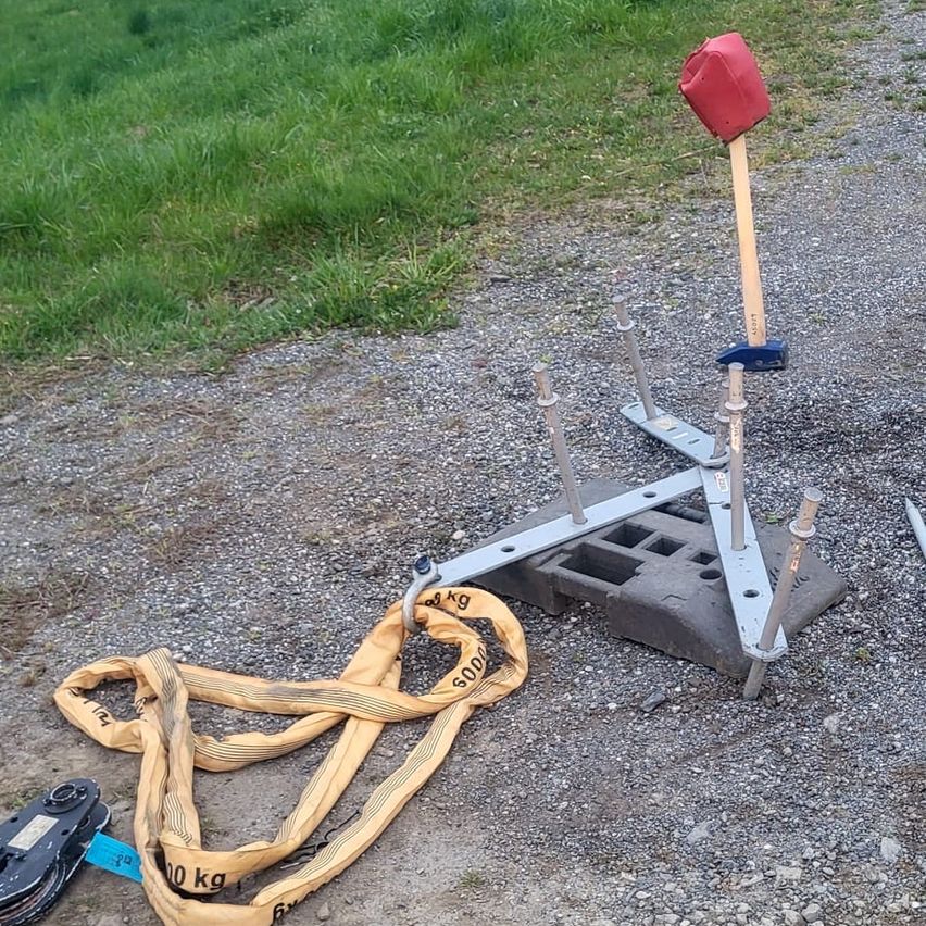A red target is set up on a gravel surface with a yellow lifting strap and metal poles, possibly for practice or training.