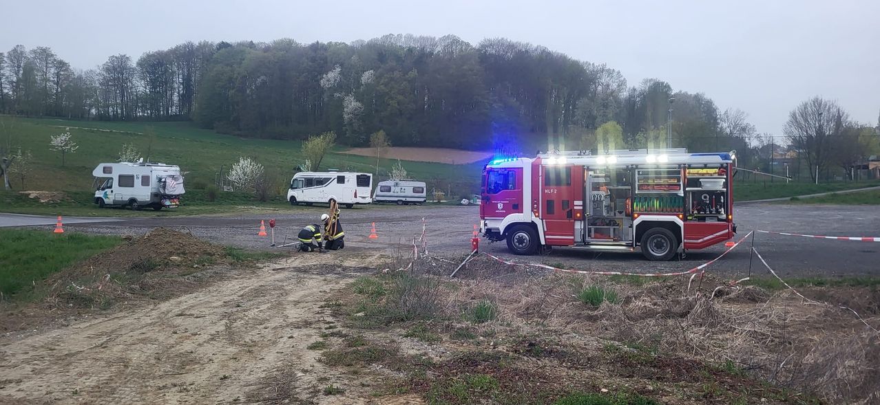 Emergency services are at the scene with a fire truck and workers attending to something on the ground. There are two campers and a field behind them.