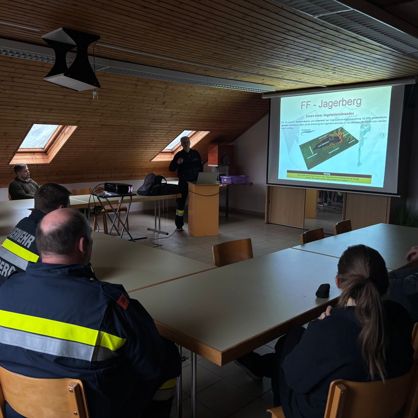 Eine Gruppe von Menschen in Uniform nimmt an einer Präsentation über Vegetationsbrände teil. Ein Mann steht vor einer Projektionsleinwand.