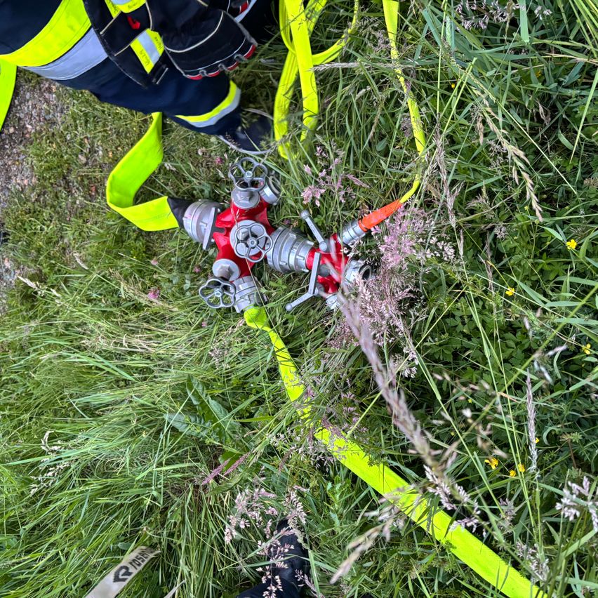 Die Sicherheitsausrüstung eines Feuerwehrmanns liegt auf dem Rasen, in der Nähe eines roten und silbernen Feuerhydranten.