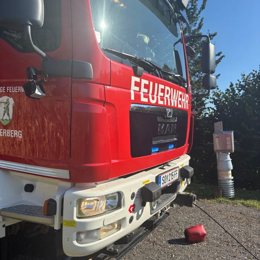 Ein roter Feuerwehrwagen mit dem Wort 'Feuerwehr' auf der Front ist am Straßenrand geparkt.